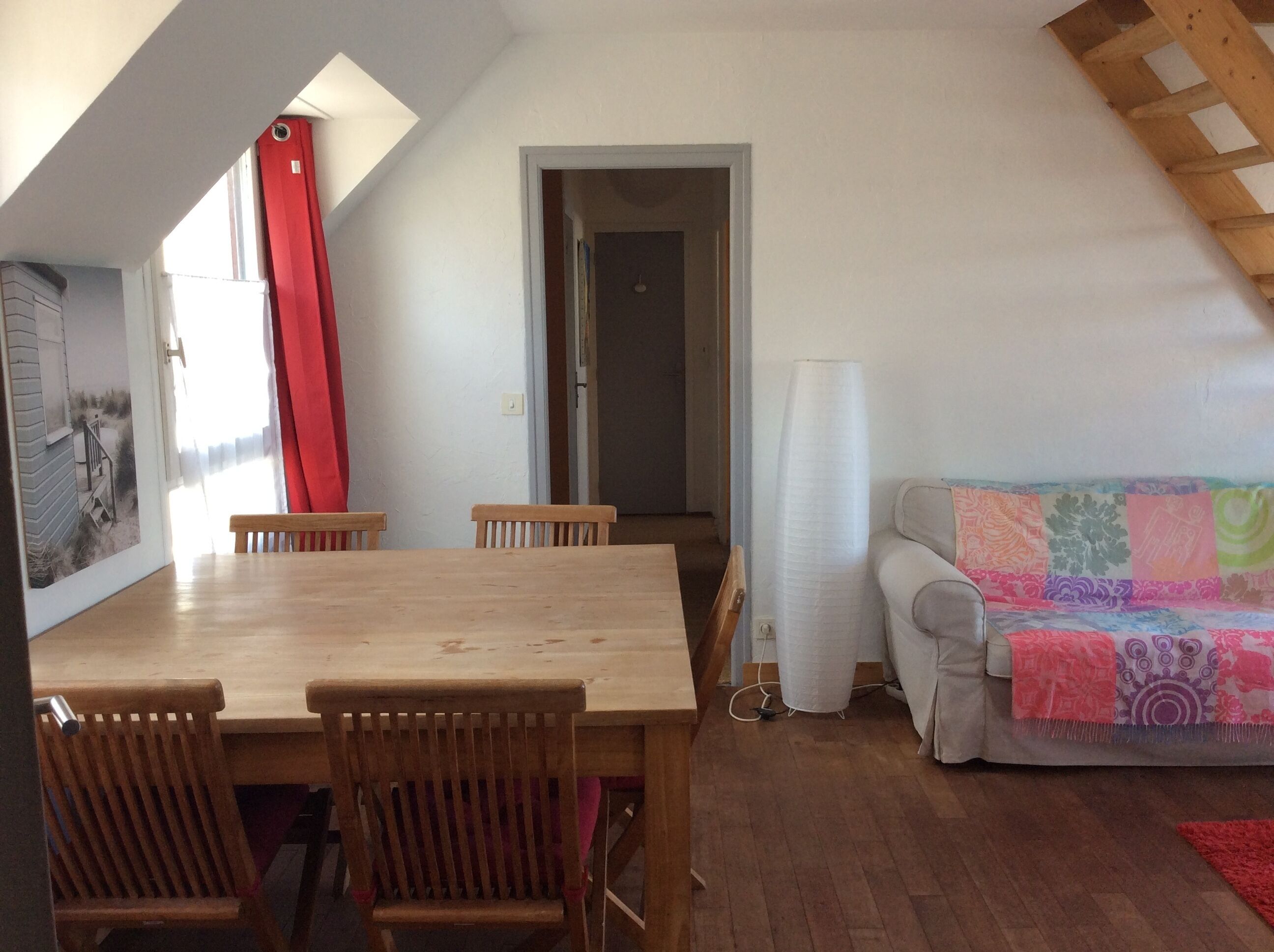 Een eethoek met een houten tafel en stoelen, een rood gordijn en een kleurrijke bank.