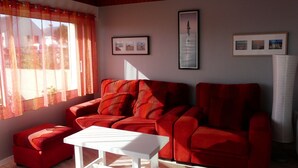 Un salon avec un canapé rouge, une table basse blanche et une fenêtre ornée de rideaux légers.