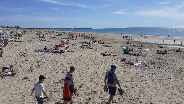 Une plage bondée où les gens se prélassent au soleil et se promènent.