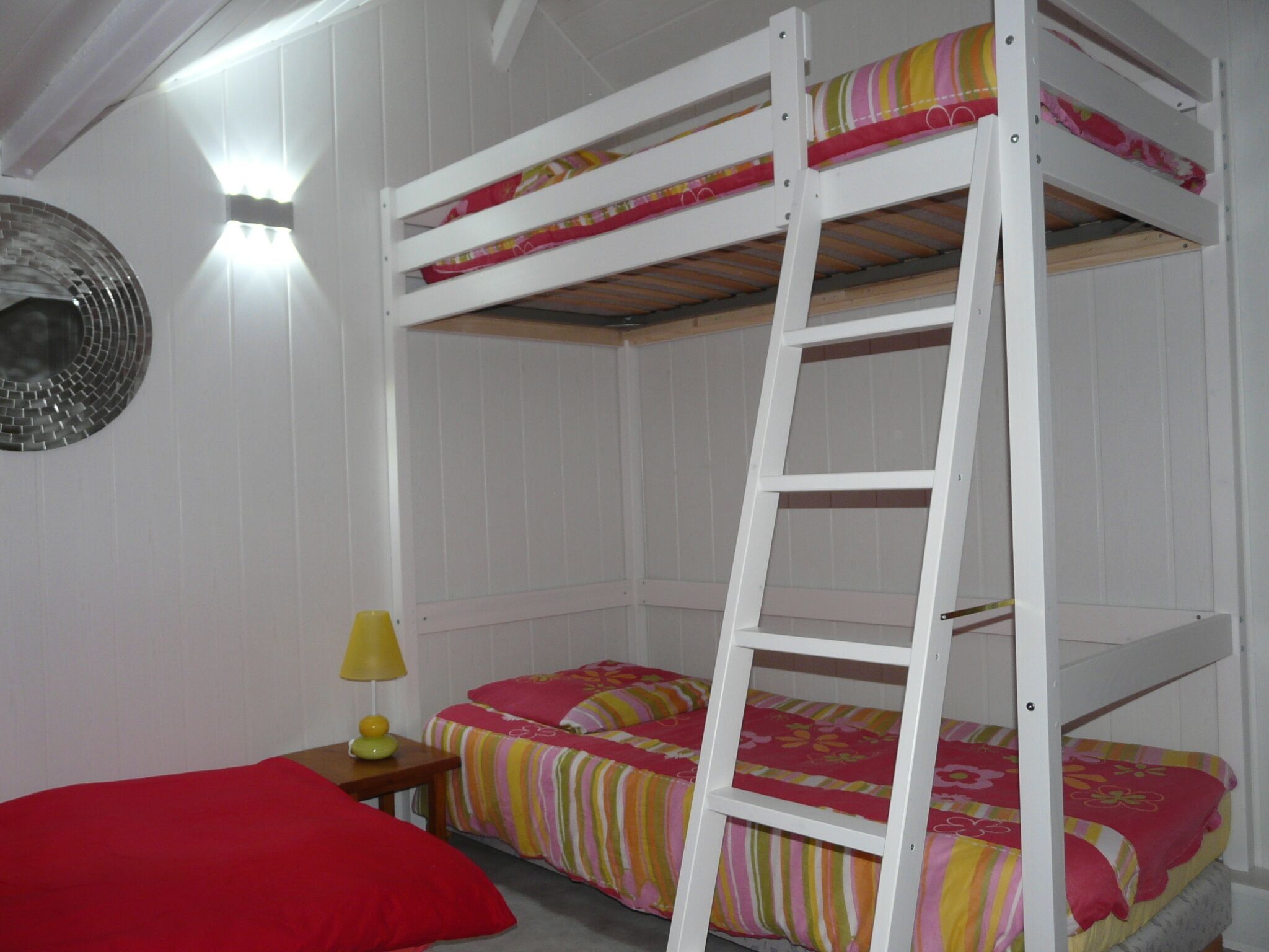 A bunk bed room with a ladder, a nightstand with a lamp, and a red pillow.