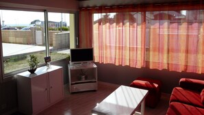 Une pièce avec un téléviseur posé sur un meuble, une table blanche et des chaises rouges.