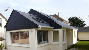 Une maison à deux étages, avec un toit sombre, de grandes fenêtres et un petit porche.