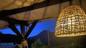 Een zwembad met een overkapte pergola, een hanglamp en een bergachtige achtergrond.