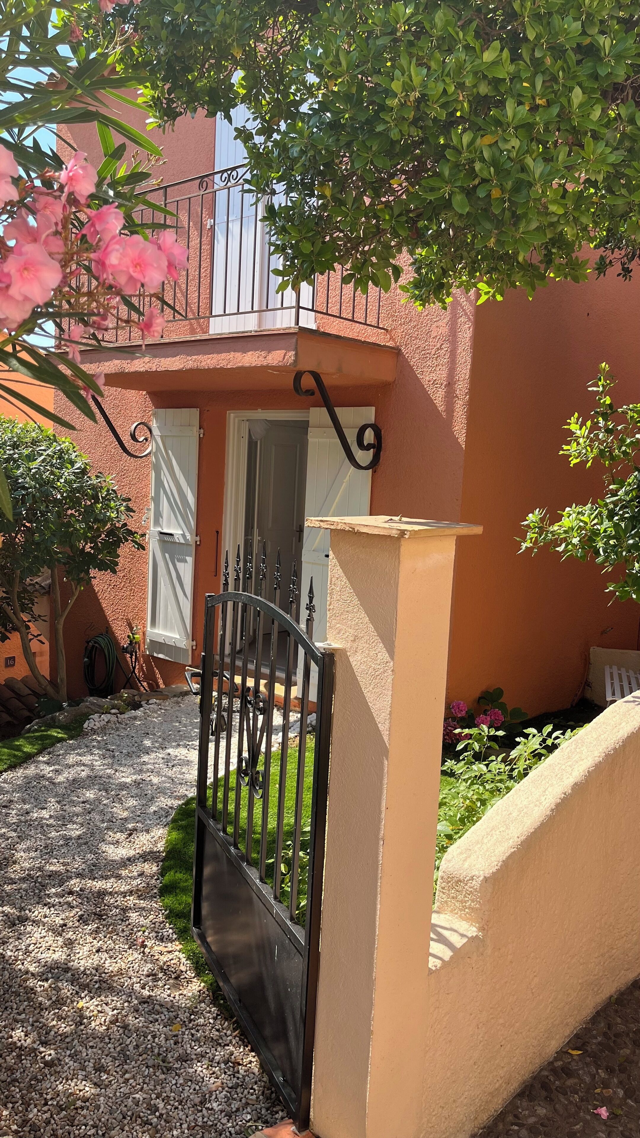 A house with a gravel driveway, a black metal gate, and a balcony with a railing.