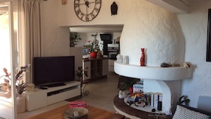 A living room with a TV, a coffee table, a fireplace, and a clock on the wall. - House in Grimaud with exceptional views of the sea and the Gulf of Saint-Tropez (GRIMAUD)