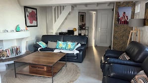 A spacious living room with a black leather sofa, a wooden coffee table, and a staircase leading to an upper level. - House in Grimaud with exceptional views of the sea and the Gulf of Saint-Tropez (GRIMAUD)