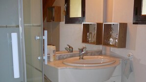 Casa de banho com cabine de chuveiro em vidro, pia branca com espelho em cima e tapete verde no chão.