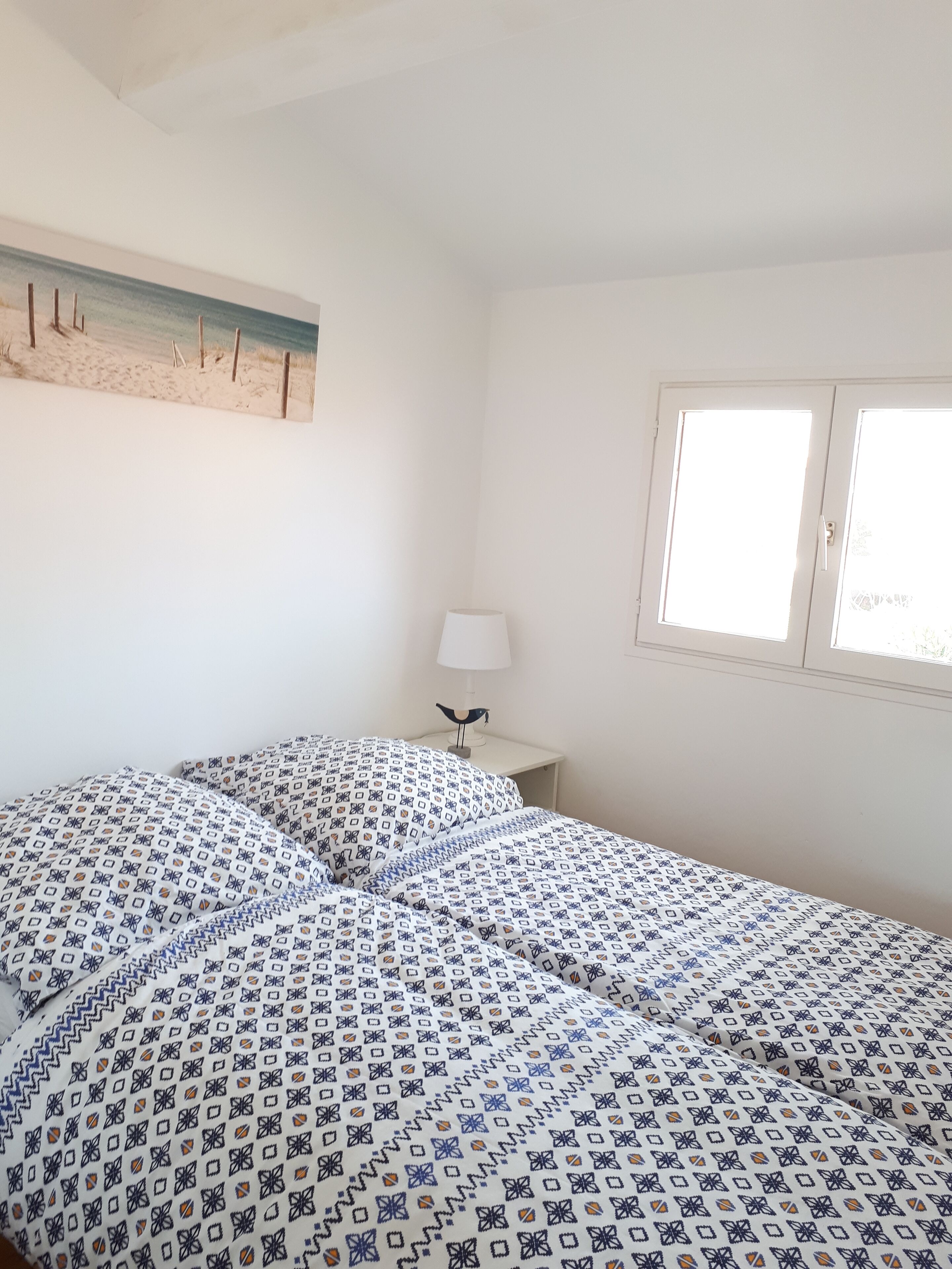 Une chambre à coucher avec un lit, une table de chevet, une lampe et une fenêtre.