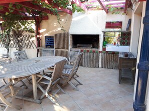 Un patio al aire libre con una mesa redonda y sillas, una parrilla y una valla de madera.