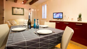 A dining area with a table set for two, a television, and a potted plant.
