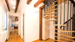 A modern interior with a wooden staircase, a kitchen area, and a hallway leading to another room.