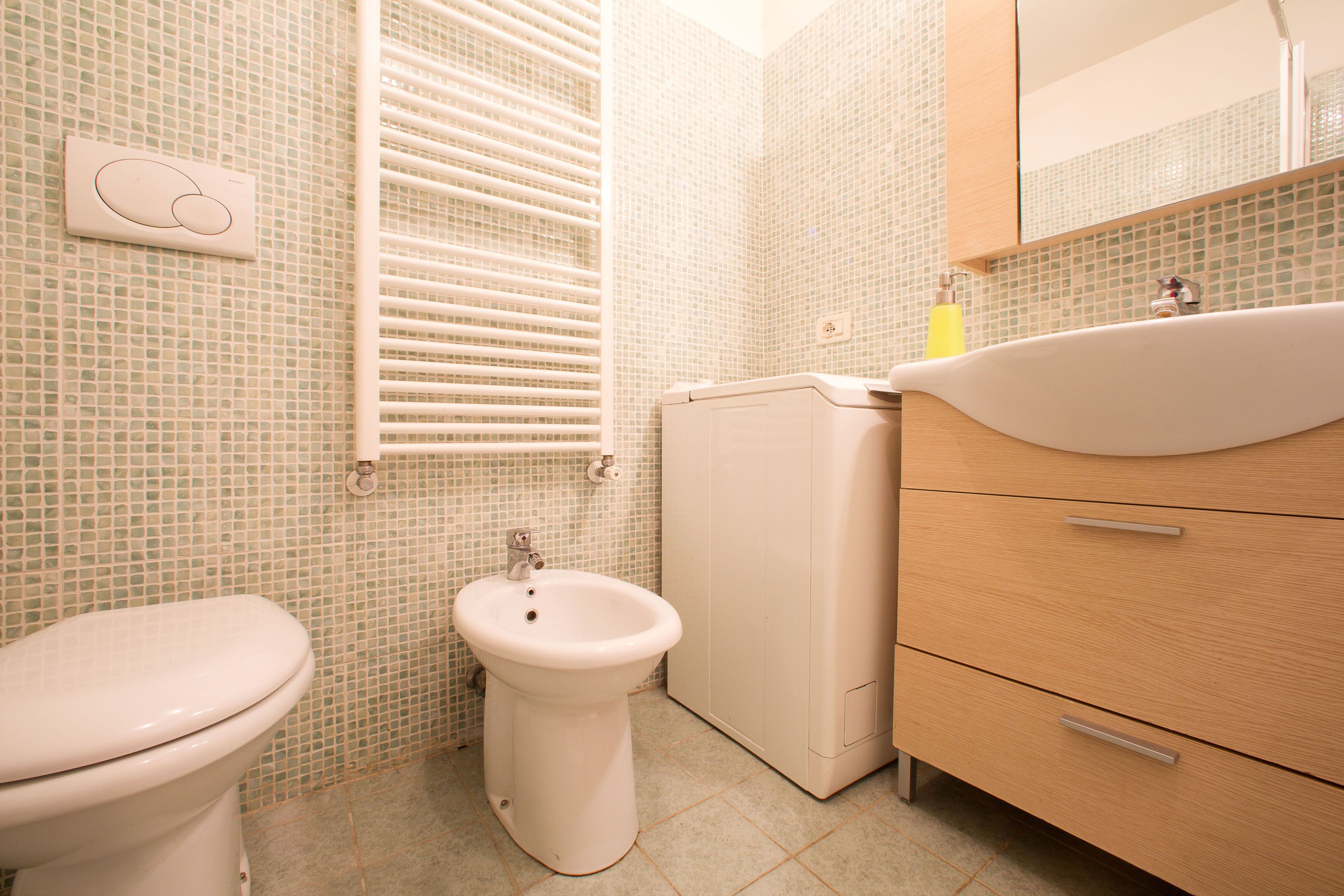 A bathroom with a toilet, bidet, and wooden cabinet with drawers.