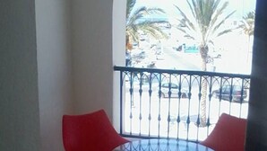 Un balcon avec une table ronde en verre et deux chaises rouges.