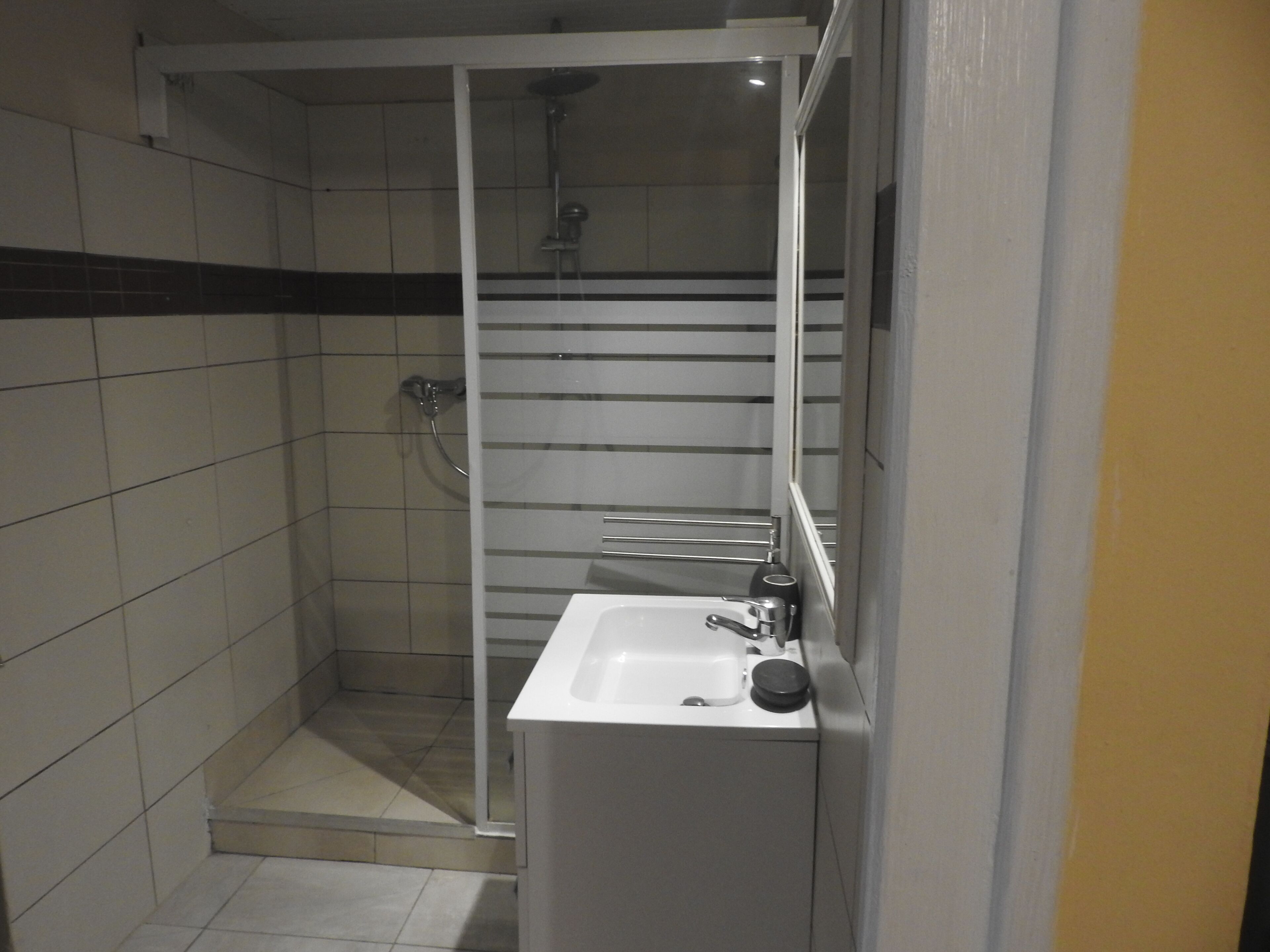 A small, enclosed shower area with a white sink and a towel rack.