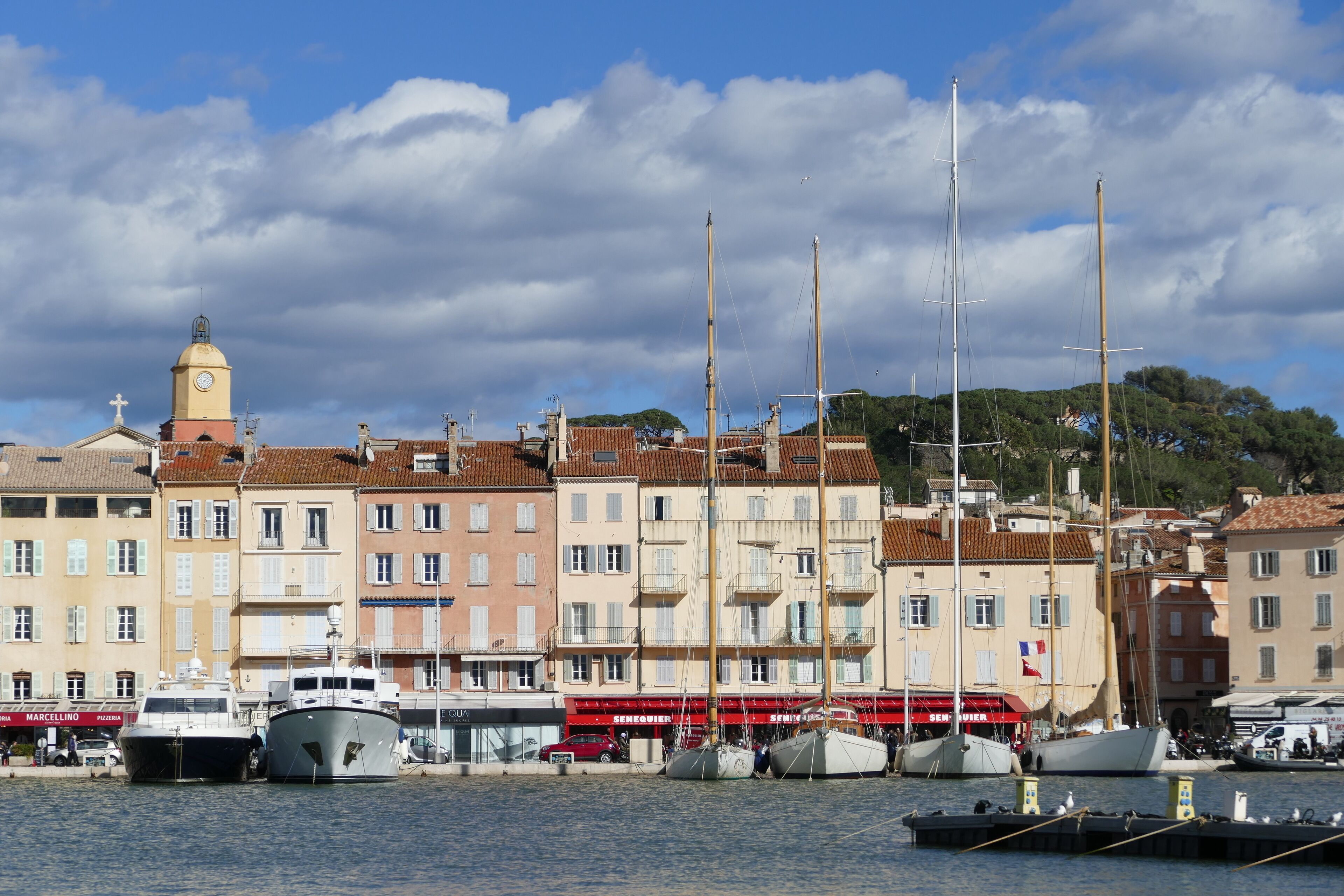 Un port avec des bateaux, une tour de l’horloge et des bâtiments dotés de balcons.
