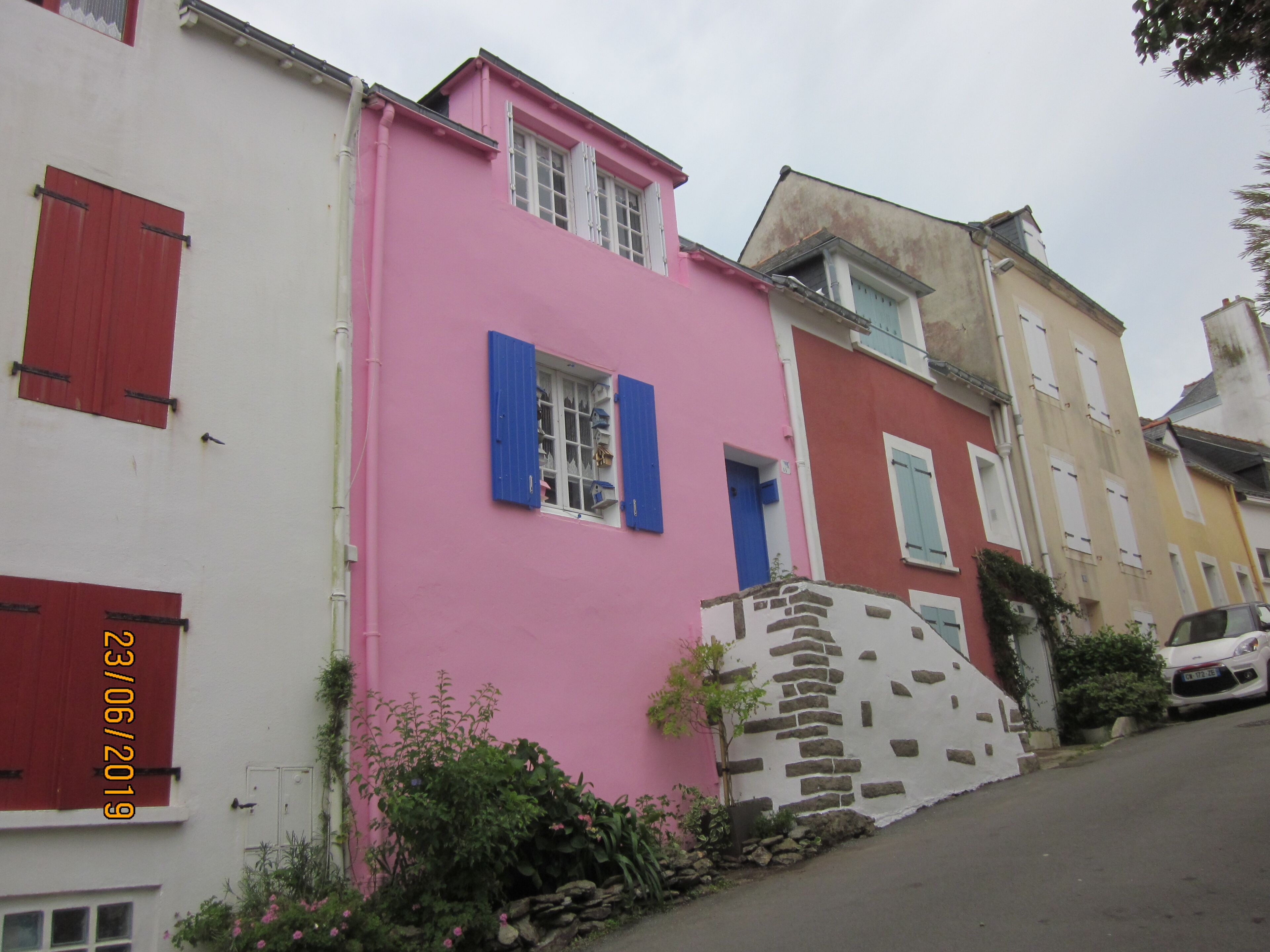 A pink building with a stone staircase, a white building with red shutters, and a yellow building with blue shutters.