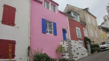 A pink building with a stone staircase, a white building with red shutters, and a yellow building with blue shutters.