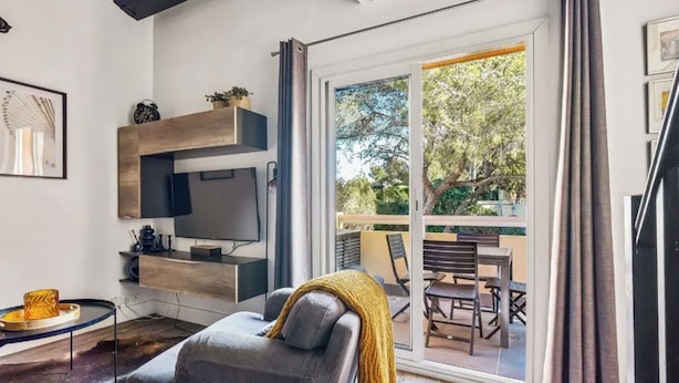 A modern living room with a sofa, a flat-screen TV, a coffee table, and a balcony with outdoor seating. - Calm & Cosy by the sea - 4 people - Fully equipped (Saint-Raphaël)