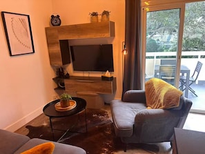A living room with a flat-screen TV, a sofa, a coffee table with a plant, and a balcony view.