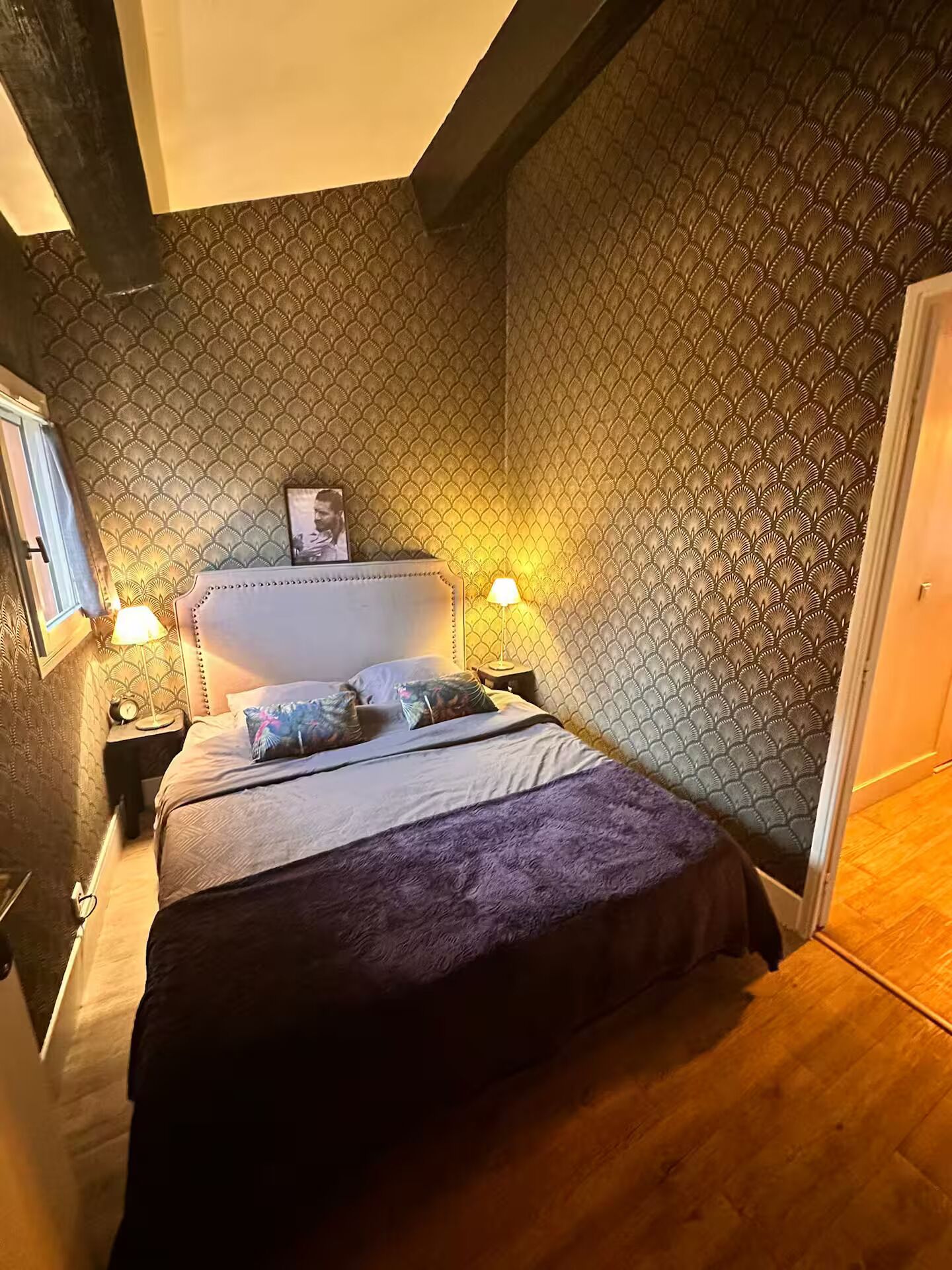 Un dormitorio con cama, dos lámparas de noche, un cabecero y una pared con estampado.