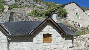 Un bâtiment en pierre doté d’un balcon, une table avec des chaises et une vue sur une colline rocheuse.