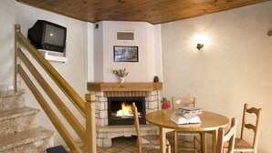 Une pièce chaleureuse avec une cheminée, un escalier en bois et un coin repas comprenant des chaises et une table.