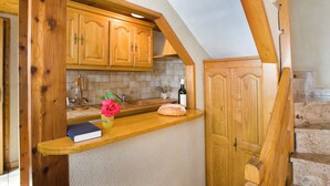 Une cuisine avec des meubles de rangement en bois, un plan de travail, un livre, un vase de fleurs et une bouteille.