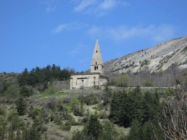 Un'antica chiesa in pietra con un campanile, immersa in un paesaggio montuoso.