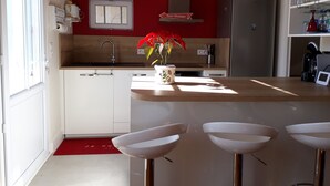 A kitchen with a red wall, white cabinets, a sink, a refrigerator, and a bar area with stools. - PIGEONNIER BEACH 5 'ON FOOT; BEACH DE PONTAILLAC 8 'all on foot (Royan)