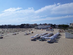 A beach with numerous sun loungers and umbrellas, a casino building, and residential buildings in the background.