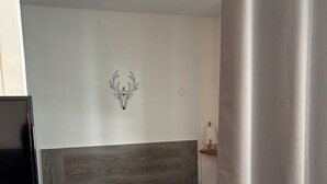 Quarto com cama, cabeceira, decoração de cabeça de veado fixada na parede e mesa de cabeceira com abajur.