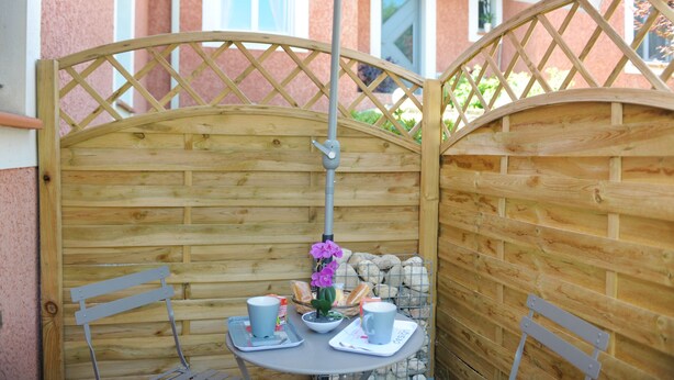 A wooden partitioned outdoor seating area with a table and chairs, a potted plant, and a basket of bread. - CALM STUDIO IN A GREEN SETTING (Montauban)