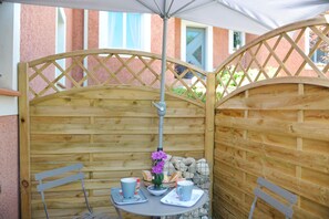 A wooden partitioned outdoor seating area with a table and chairs, a potted plant, and a basket of bread. - CALM STUDIO IN A GREEN SETTING (Montauban)
