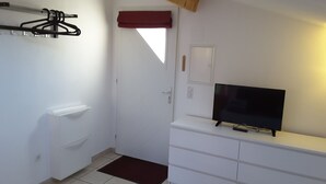 A small, clean room with a white wardrobe, a television on a white cabinet, a red curtain, and a tiled floor. - CALM STUDIO IN A GREEN SETTING (Montauban)