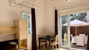 Een moderne woonkamer met een flatscreen-tv, houten wandplanken, een eethoek met een tafel en stoelen, en een schuifdeur die leidt naar een buitenpatio.