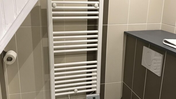 Une salle de bain avec des toilettes blanches, un porte-serviettes et un radiateur fixé au mur.