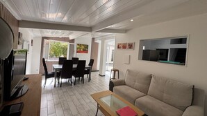 A modern living room with a sofa, a glass-top coffee table, a dining area with chairs, a TV, and a refrigerator. - Near Soulac/mer, house 3 bedrooms, sleeps 6, heated indoor pool (Grayan-et-l'Hôpital)