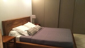 Ein Einzelbett mit Holzrahmen, einem weißen und gemusterten Kopfkissen, einer violetten Decke und einem Nachttisch mit Lampe.