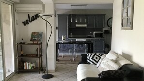 Ein Wohnzimmer mit Sofa, Couchtisch und Stehlampe. Es gibt eine Küchenzeile mit Schränken und einer Mikrowelle.