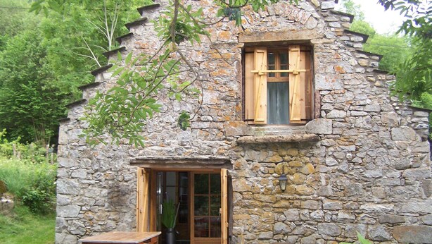 Une petite maison en pierre avec une porte en bois, une petite fenêtre avec des volets et une terrasse avec une table et des chaises.