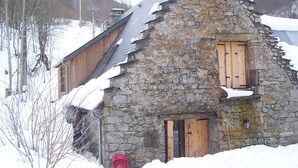 Un bâtiment en pierre, doté de volets en bois et d’un toit en pente, entouré de neige.