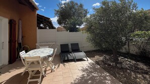 Une terrasse avec une table et des chaises, un petit arbre et un sol carrelé.