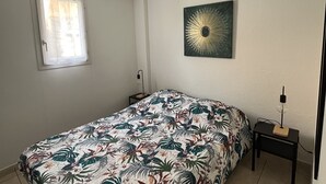 Une chambre à coucher avec un lit, une table de chevet, une horloge murale et une fenêtre avec des rideaux.
