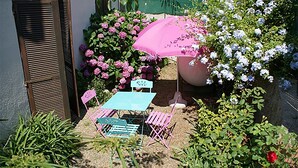 Ein Garten-Terrasse mit Tisch und Stühlen, umgeben von blühenden Pflanzen und einem großen Sonnenschirm.