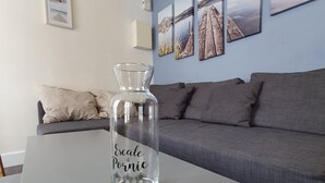 Eine klare Glasflasche mit Beschriftung auf einem weißen Tisch in einem Raum mit grauem Sofa und Wandbildern.