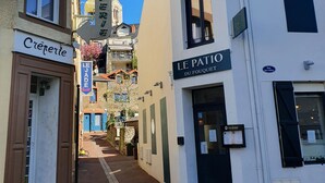 Eine schmale Straße, gesäumt von Häusern, darunter ein Café namens 'Creperie' und ein Geschäft namens 'Le Patio'.