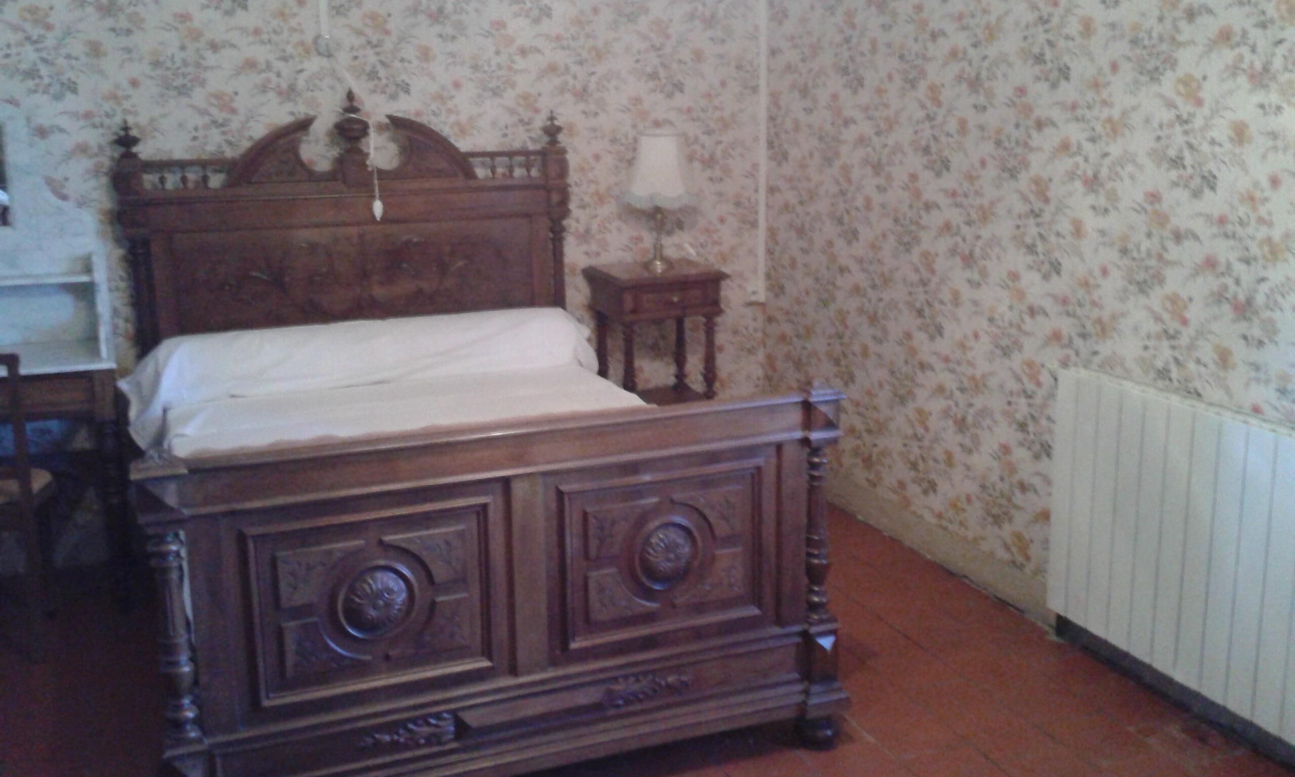 Una cama de madera con cabecera, una mesita de noche con lámpara y papel tapiz floral.