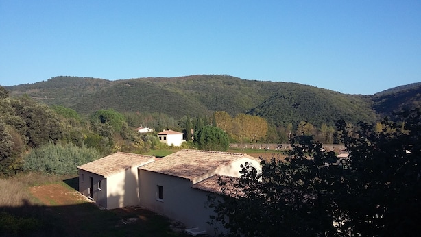 Paisaje rural con una construcción pequeña con techo de tejas, rodeada de vegetación y colinas.