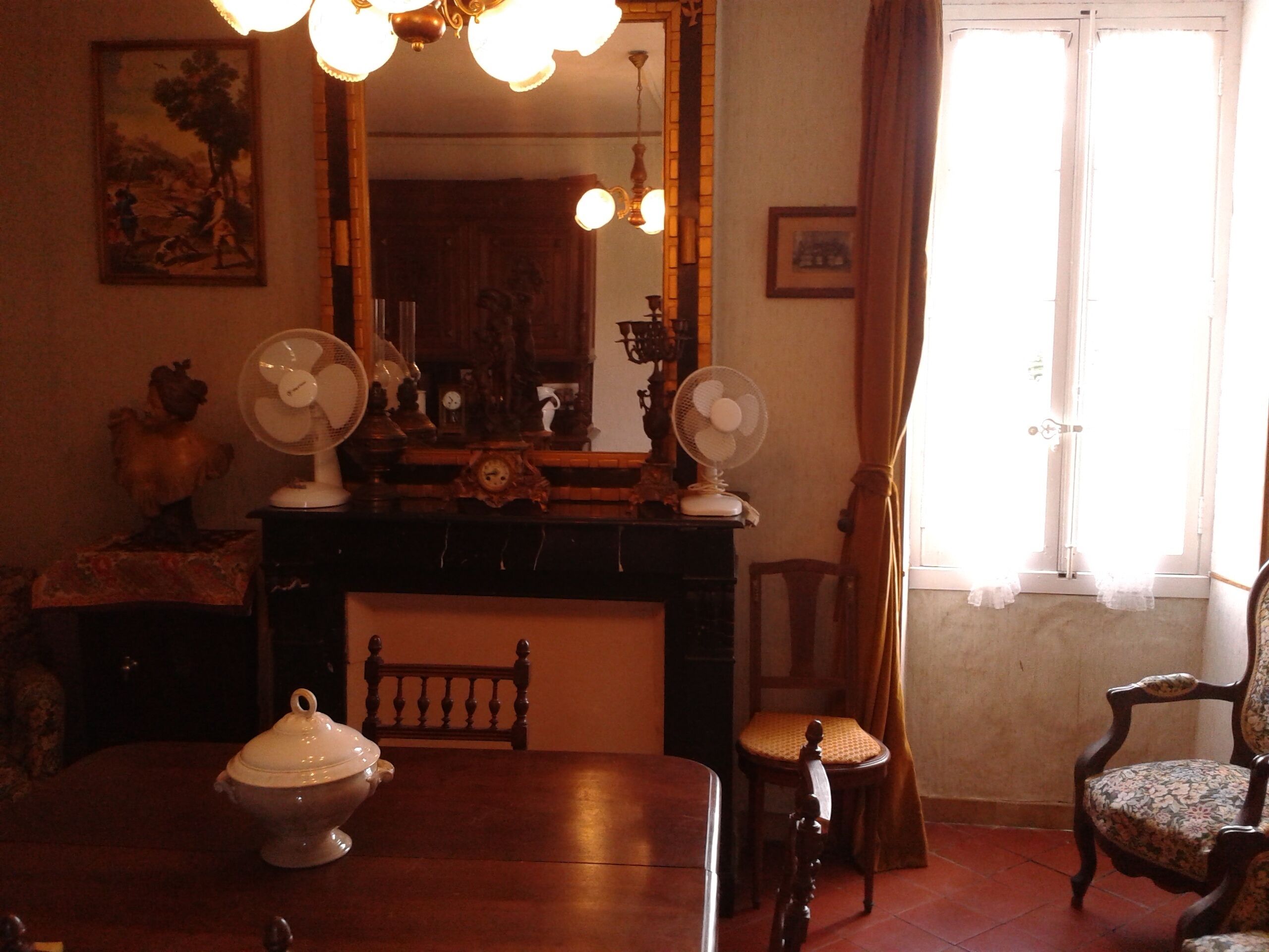 A room with a fireplace, two wall-mounted fans, a wooden table, a chair, and a large mirror.