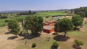 Una villa rodeada de exuberante vegetación y campos, con una piscina visible al fondo.